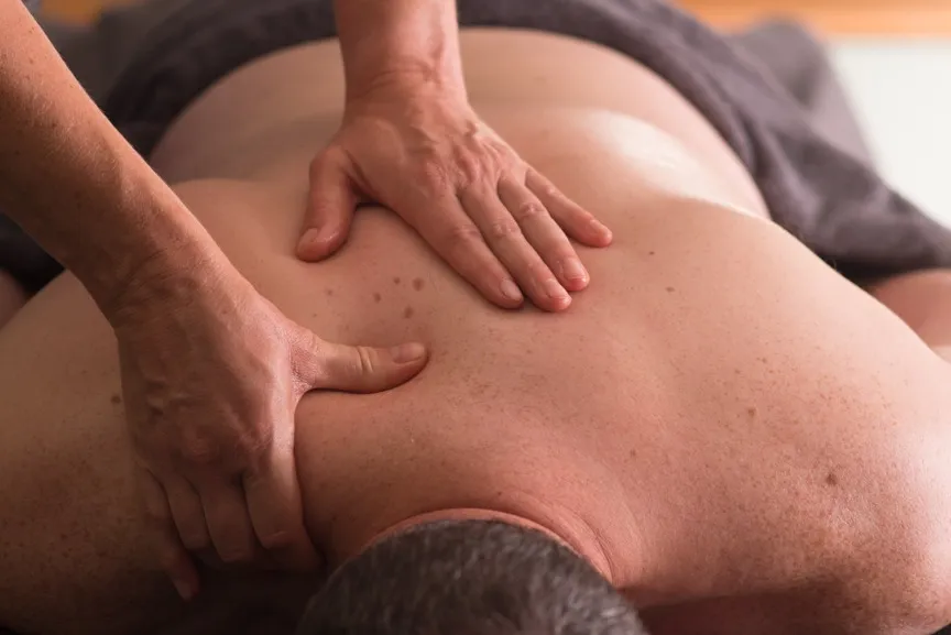 Sports massage therapist applying thumb pressure along a client's back