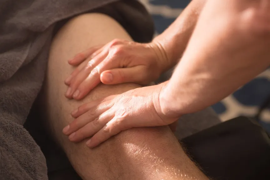 A sports massage therapist working along a client's hamstring with both hands